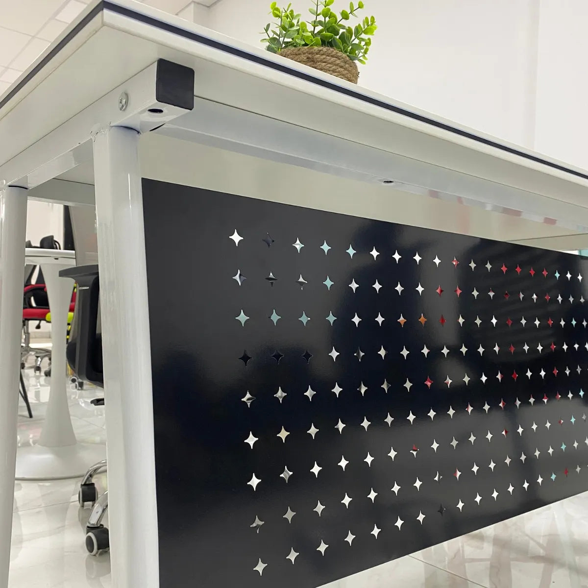 Modern office desk with star-patterned screen and plant on a white floor.